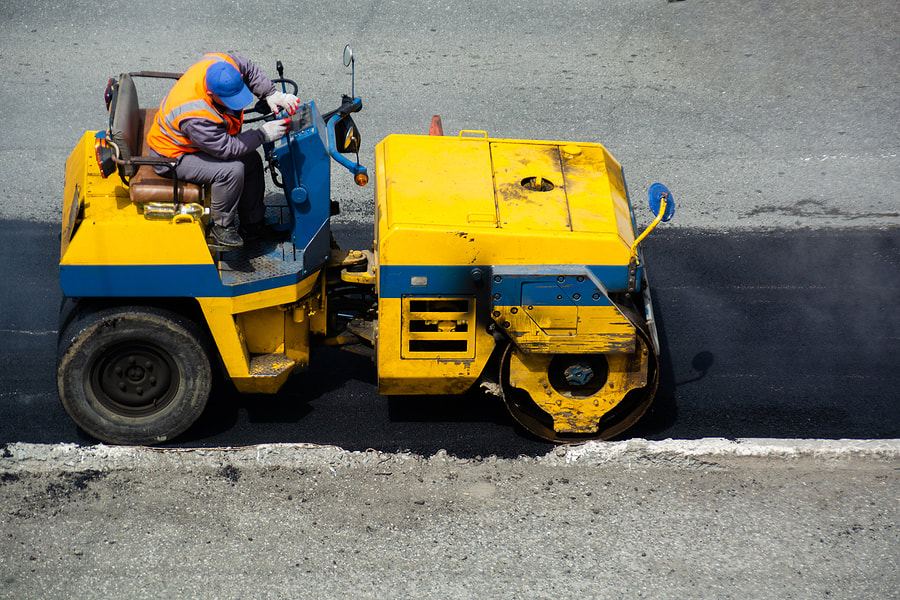 worker on the roller truck flattens the asphalt
