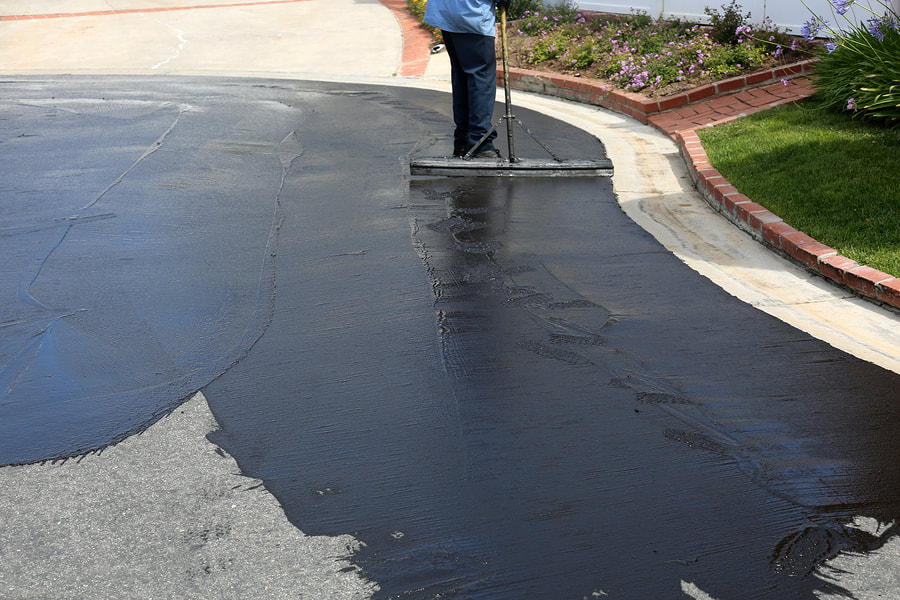 worker putting seal coating on the driveway 